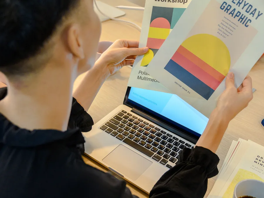 Printed graphic design brochures being reviewed beside a laptop
