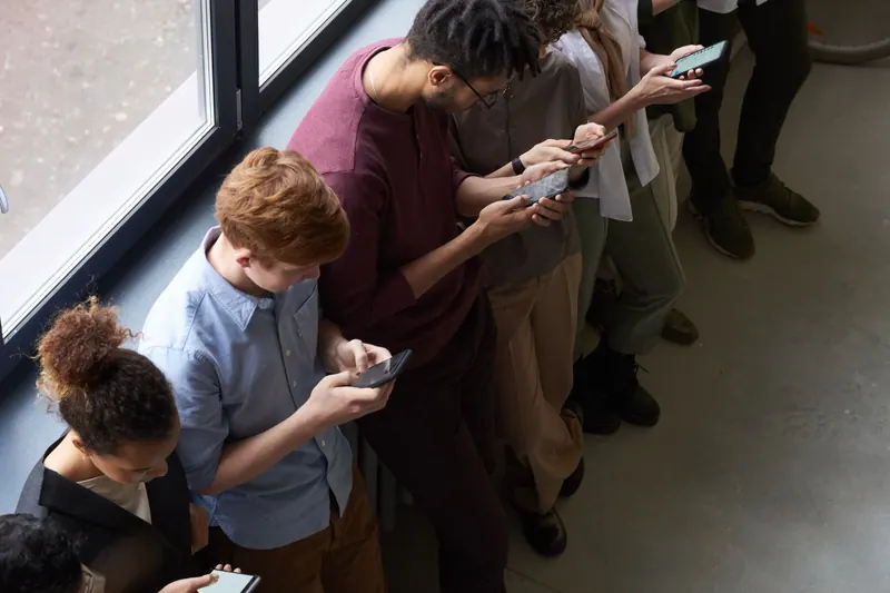 People using smartphones together beside a window